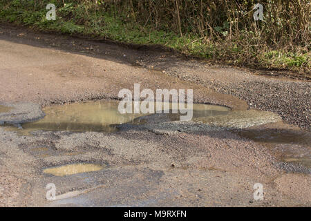 Potholes with upwelling water under the road after rain that have developed on a country lane in North Dorset UK Stock Photo