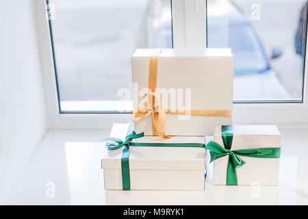 Set of white gift boxes with different colored ribbons on windowsill Stock Photo