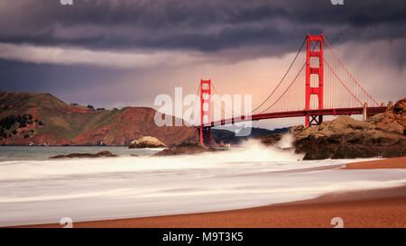 Dramatic mid-afternoon stormy sky over Golden Gate Bridge with crashing waves on Baker Beach