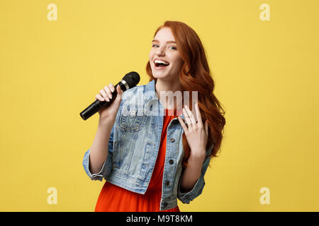 Lifestyle and People Concept: Expressive beauty ginger hair model girl in casual jean cloth singer with a microphone. Stock Photo