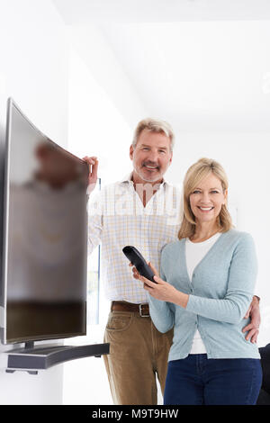 Portrait Of Mature Couple With New Curved Screen Television At Home
