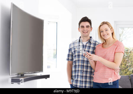 Portrait Of Young Couple With New Curved Screen Television At Home