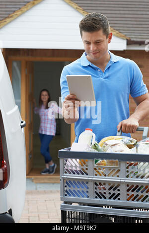 Driver Delivering Online Grocery Order To House Using Digital Tablet Stock Photo