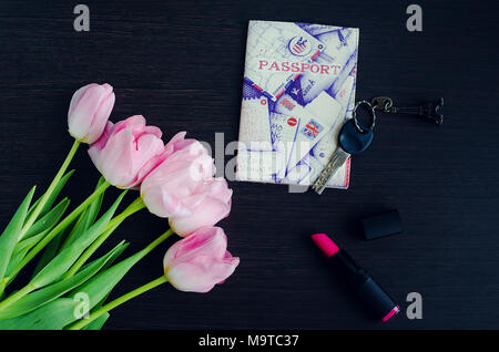 Bouquet of pink tulips with passport, lipstick and key on dark wooden background. Key with Eiffel Tower. Travel concept. Top view. Stock Photo