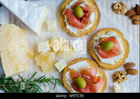Delicious bruschetta with prosciutto and olives with cheese Parmesan and Bree, rosemary and nuts. Italian appetizer. Top view. Stock Photo