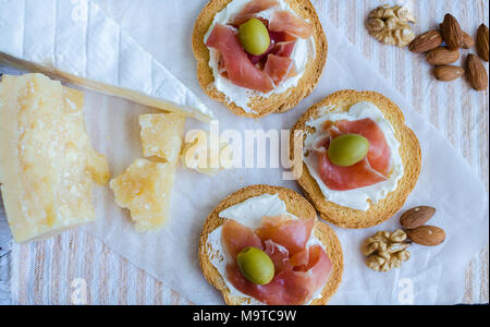 Delicious bruschetta with prosciutto and olives with cheese Parmesan and Bree, and nuts. Italian appetizer. Top view. Stock Photo