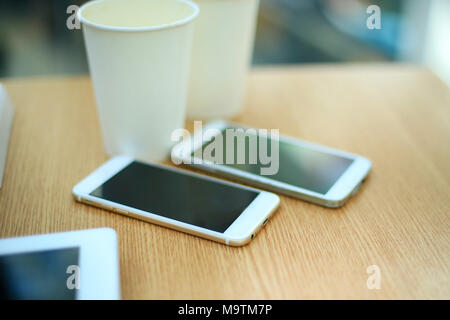 Two white mobile phones with tablet on wooden table background, blank screen electronic device with copy space. Stock Photo