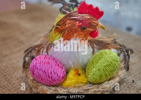 Happy Easter. Easter chick decoration in a nest hatches colorful easter eggs on a natural jute fabric background. Stock Photo
