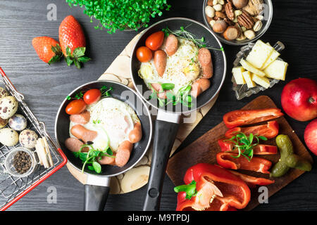 English health breakfast for two. Fried eggs with sausages in a frying pan with spices and fresh vegetables. Stock Photo