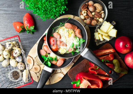 English health breakfast for two. Fried eggs with sausages in a frying pan with spices and fresh vegetables. Stock Photo