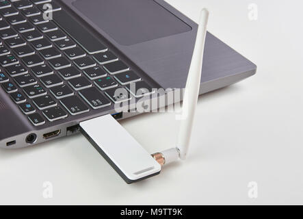 Silver laptop with USB modem plugged in with an antenna, on a white board table Stock Photo