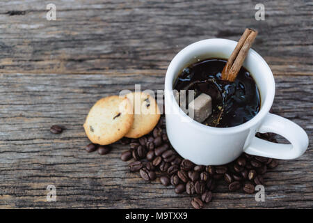 Brown sugar cube falling  into hot coffee mug with coffee beans and cookies on wood background Stock Photo