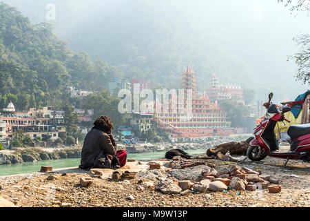 poor man sits on the banks of the Ganges river and looks towards the temple Tera Manzil Temple. Morning prayer before the Holy place. Meditation in Ri Stock Photo