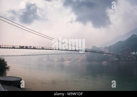 bridge Lakshman Jhula over the river Ganges in the city of rishies, India. evening dark landscape. Houses on the high slopes of the Himalayas Stock Photo