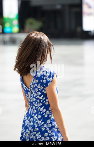Rear view of a woman wearing blur floral dress walking in the street Stock Photo