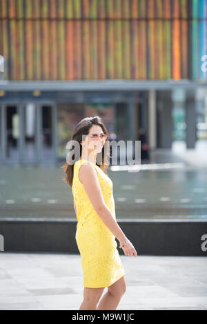 Happy beautiful woman wearing yellow summer dress and sunglasses walking outdoors smiling Stock Photo
