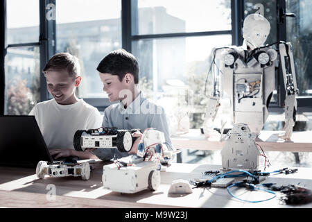 Joyful children working in workshop and programming robotic machines Stock Photo