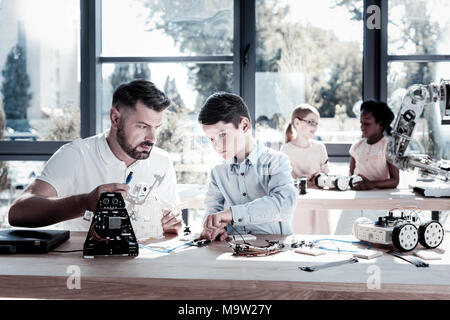 Focused youngster working on robot with his teacher Stock Photo