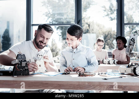 Joyful teacher and student smiling while working on robotic machine Stock Photo