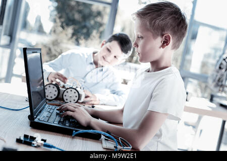 Intelligent schoolchildren working on laptop after constructing robot Stock Photo