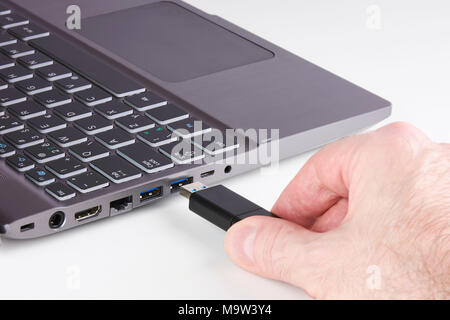 Silver laptop and male hand holding USB Flash disk and plugging into slot - on white background Stock Photo
