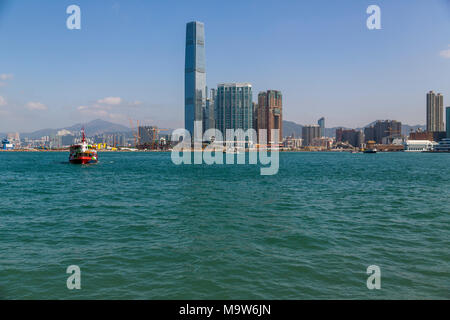 The International Commerce Centre stands proud in West Kowloon, amid ongoing construction work. A ferry crosses Victoria Harbour to Hong Kong Island. Stock Photo