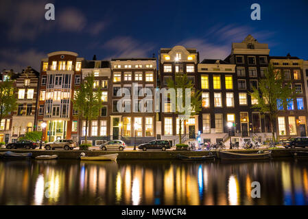 Beautiful night in Amsterdam. Night illumination of buildings and boats near the water in the canal. Stock Photo