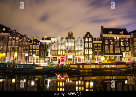 Beautiful night in Amsterdam. Night illumination of buildings and boats near the water in the canal. Stock Photo