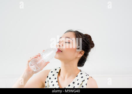 Young beautiful asian woman holding a glass of water while sitting at home Stock Photo