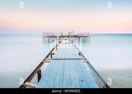 Perspective view of a old pier in a completely calm sea with gentle sky and clouds. Long exposure and soft colors Stock Photo