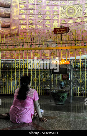 A faithful Buddhist prays in front of the enormous feet of the reclining Buddha in the Chaukhtatgyi Pagoda in Yangon Stock Photo