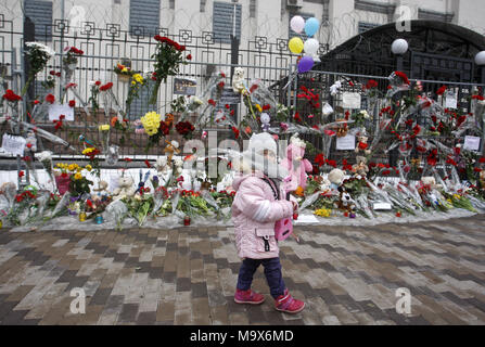 Kiev, Ukraine. 28th Mar, 2018. A little girl walks past near flowers and toys in memory for the victims of the fire in the shopping mall 'Zimnyaya Vishnya' in the West Siberian city of Kemerovo, in front the Russian Embassy in Kiev, Ukraine, on 28 March 2018. Reports state that at least 64 people, including 41 children, died in the fatal incident on 25 March. Credit: Serg Glovny/ZUMA Wire/Alamy Live News