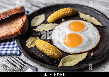 Fried eggs in a frying pan. Rye toast and pickled cucumber next to fried eggs. Stock Photo