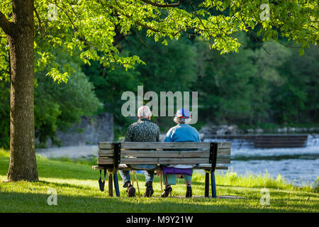 Senior couple sitting on a bench with river and waterfall in background. Stock Photo