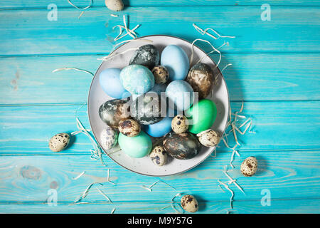 painted eggs on plate, quail and chicken eggs, paint and brush on blue wood background, Easter decorations. Stock Photo