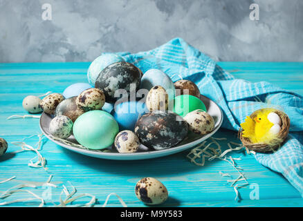 painted eggs on plate, quail and chicken eggs, paint and brush on blue wood background, Easter decorations. Stock Photo