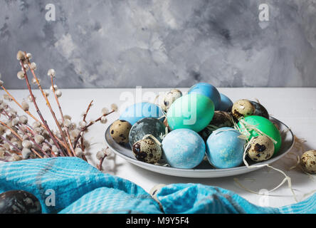 painted eggs on plate, quail and chicken eggs, paint and brush on white wood background, Easter decorations. Stock Photo