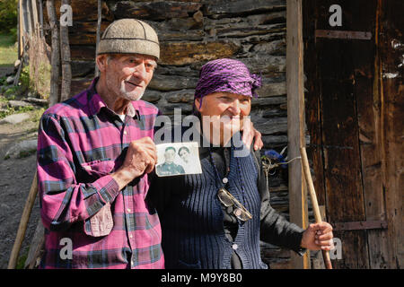 An elderly married couple standing outside an old stone shed display a photograph of themselves, taken in 1958, Ushguli, Upper Svaneti, Georgia Stock Photo