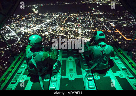 (Left to right) Senior Airman Stephen Clark and Airman 1st Class Matthew Pfeffer, 36th Airlift Squadron C-130J loadmasters, sit on the open ramp of a C-130J Super Hercules flying near Yokota Air Base, Japan, March 26, 2018, before conducting a simulated airdrop over Yokota. Yokota aircrews regularly conduct night flying operations to ensure they are prepared for a variety of contingencies throughout the Indo-Asia Pacific region. (U.S. Air Force photo by Yasuo Osakabe) Stock Photo