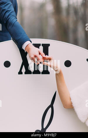 Happy wedding couple softly holding hands at the big vintage clocks in  autumn forest close up. Creative decorations Stock Photo