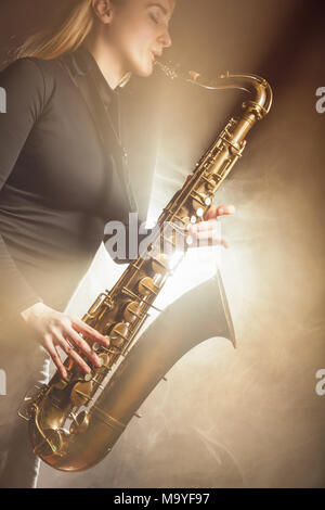 Saxophone player. Woman with saxophone on a beige background. Fog in the background. Studio shot Stock Photo