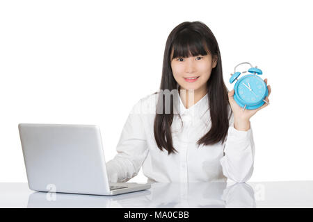 Beautiful Asian woman sitting at a desk smiling with a blue alarm clock isolated on a white background Stock Photo