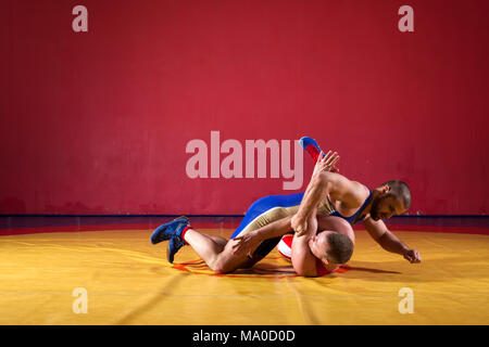 Two greco-roman  wrestlers in red and blue uniform wrestling   on a yellow wrestling carpet in the gym Stock Photo