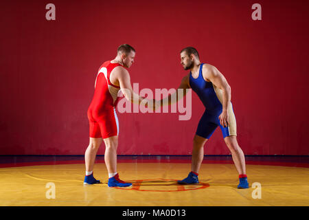 Two greco-roman  wrestlers in red and blue uniform shake hands before each other  on a yellow wrestling carpet in the gym Stock Photo