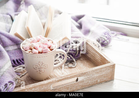 Coffee cup, open book, marshmallow and plaid on a window sill in winter. Cozy home breakfast concept