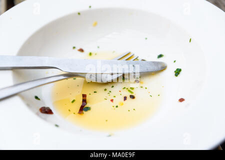 Empty white plate, knife and fork with olive oil, herbs and chili flakes leftover Stock Photo