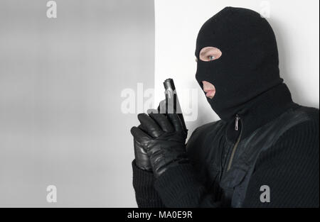 Armed man in balaclava hiding behind a wall. Stock Photo