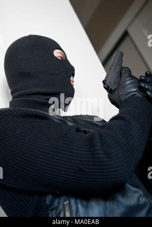 Armed man in balaclava hiding behind a wall. Stock Photo