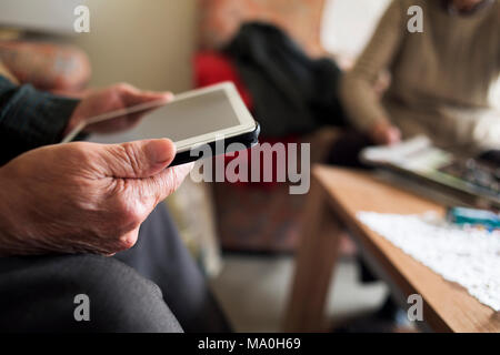 closeup of an old caucasian man using a tablet and an old caucasian man reading a magazine, sitting both in a couch Stock Photo