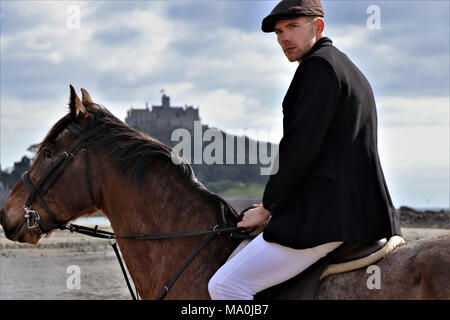 Handsome Horse Rider on horseback riding on beach in front of ancient building of St Michael's Mount, Stock Photo